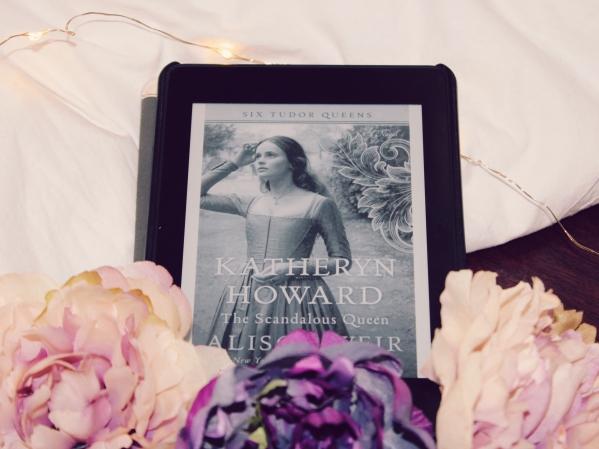 Katheryn Howard on kindle behind front of pink and purple roses with a white background and twinkle lights