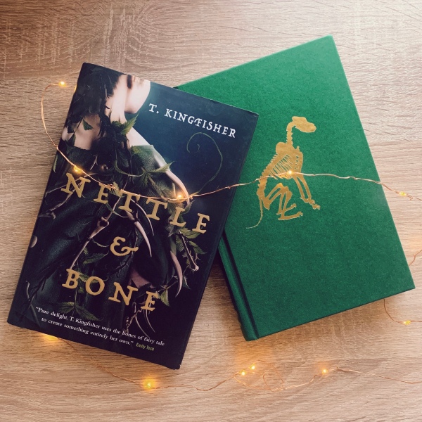 The dust jacket angled off of the hardbound book to display the gold embossed figure of a skeleton dog on the green case. Surrounded by twinkle lights on a light wood background.