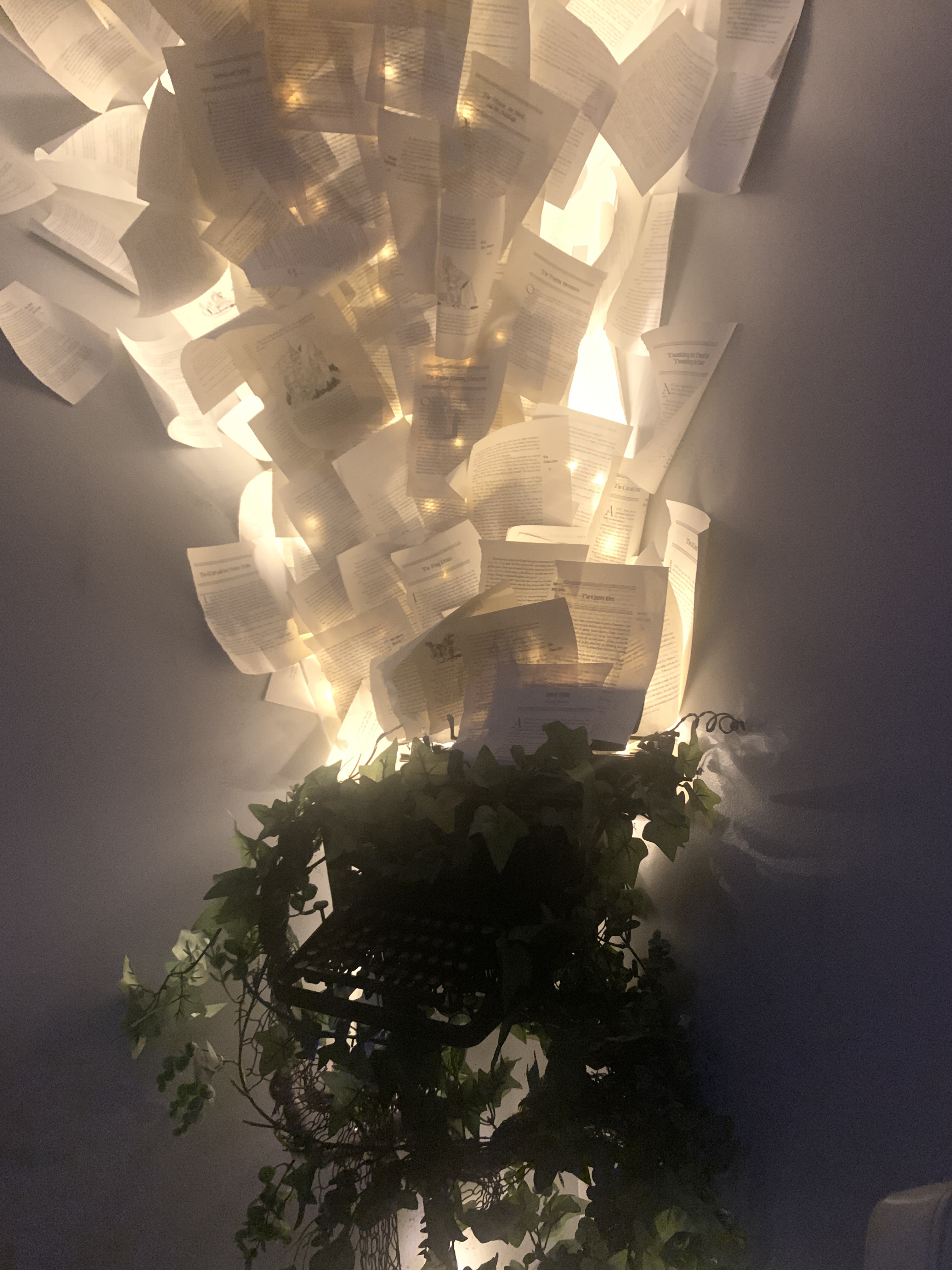 letters exploding up a wall with lights behind them allowing them to glow, they coming out of a skeleton typewriter with fake leaves covering it