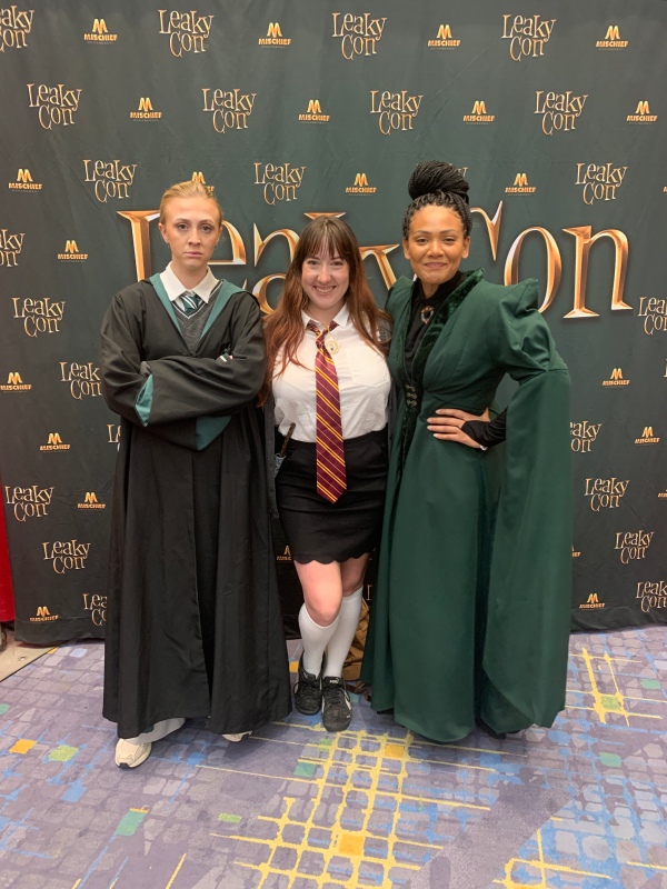 Emily Wallbank dressed as Draco Malfoy, me dressed as Hermione Granger, and Chanel Williams dressed as Minerva McGonnagall posing in front of a LeakyCon backdrop.