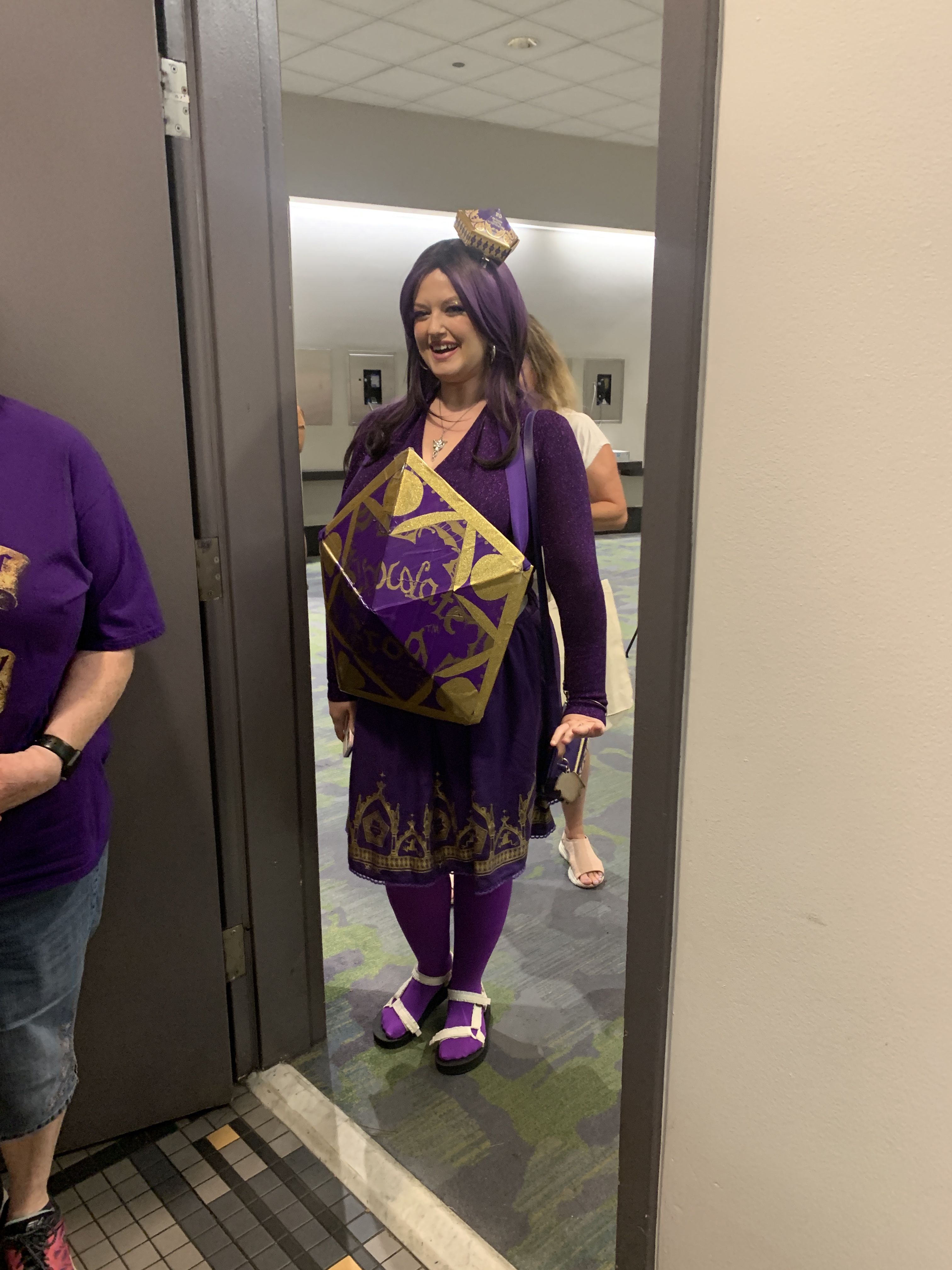 A woman dressed in cosplay as a chocolate frog wearing all purple and with a purple wig.